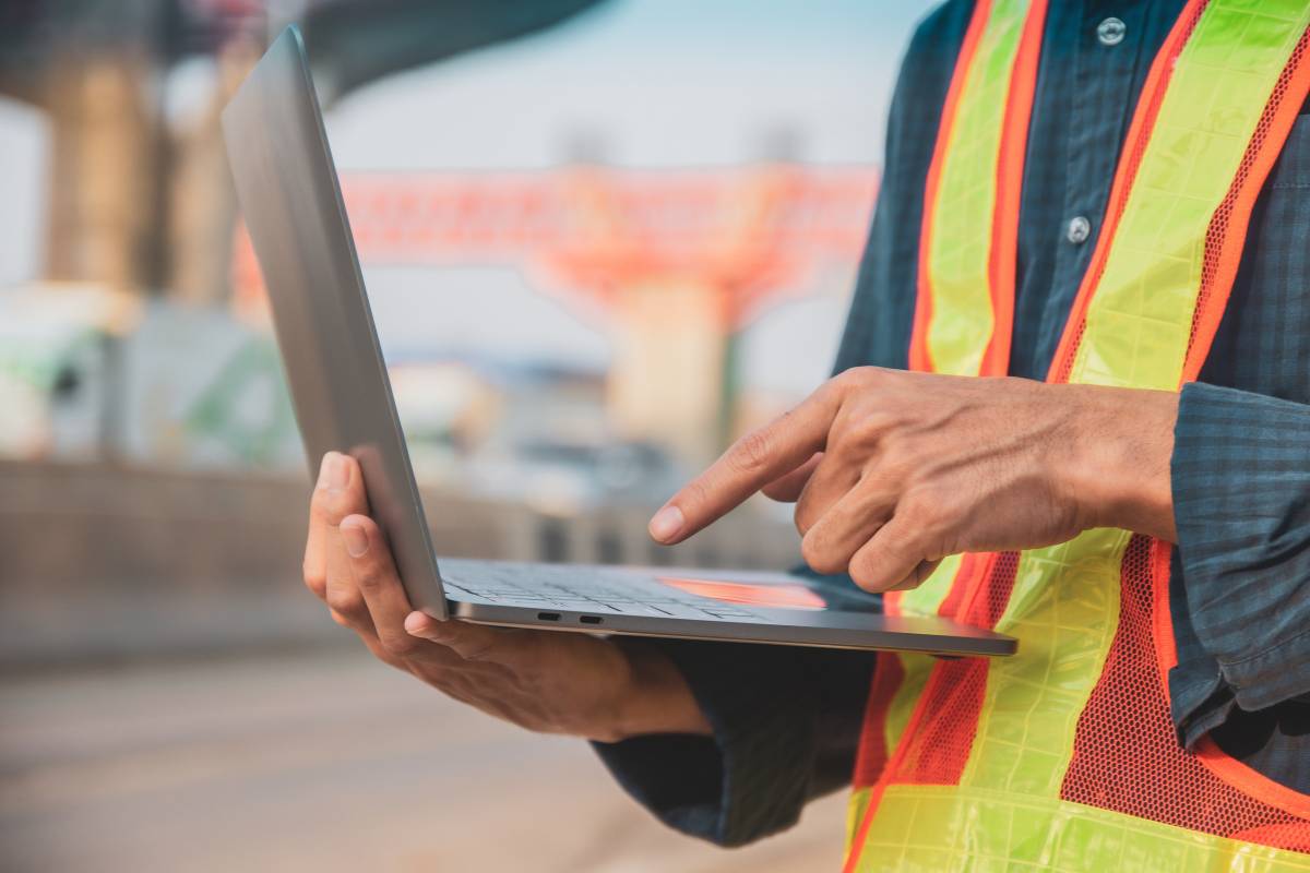 Construction technician using test lab management software on laptop at job site