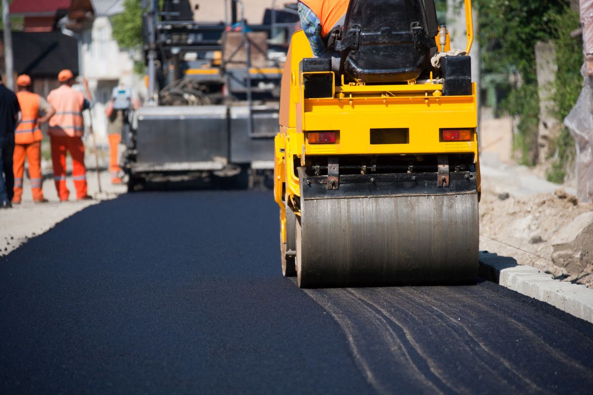 Road roller compacting fresh asphalt on a roadway under construction.